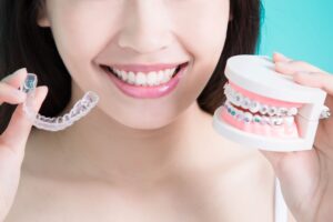 Nose-to-collarbone view of woman holding fake teeth with braces in one hand and Invisalign in the other